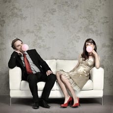 Dressed up couple sitting on couch blowing big bubbles using gum