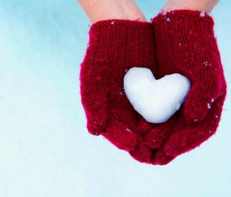 Person wearing gloves holding a heart shaped snow ball