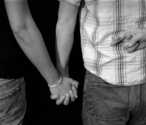 Couple holding hands with man crossing his fingers behind his back