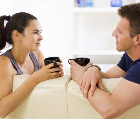 Couple sitting on couch talking and drinking coffee