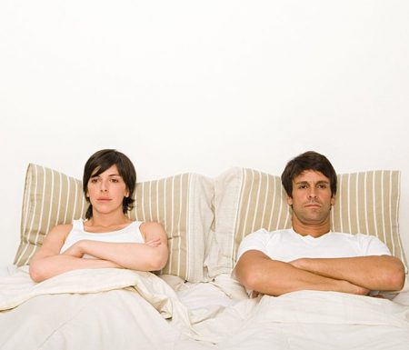 Husband and wife in bed looking upset at each other
