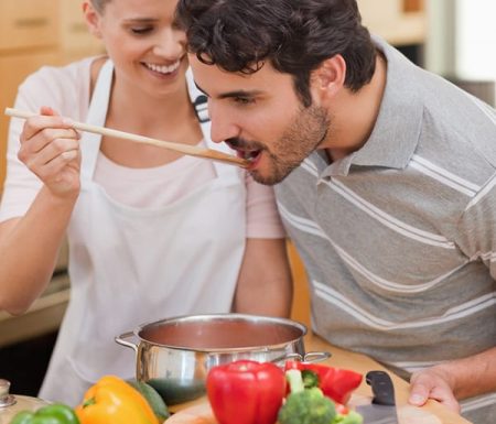 Couple cooking together. Women holding spoon up for the man taste the sauce.