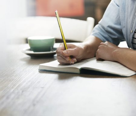 Man writing in a notebook with coffee by his side