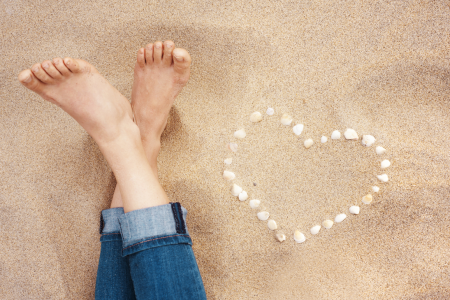 Lady's feet at the beach with shells making a heart shape