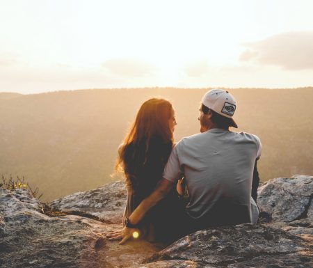 Couple sitting on top of mountain looking at a sunset