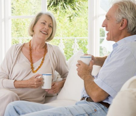 Older couple sitting on a couch drinking coffee enjoying conversation with one another