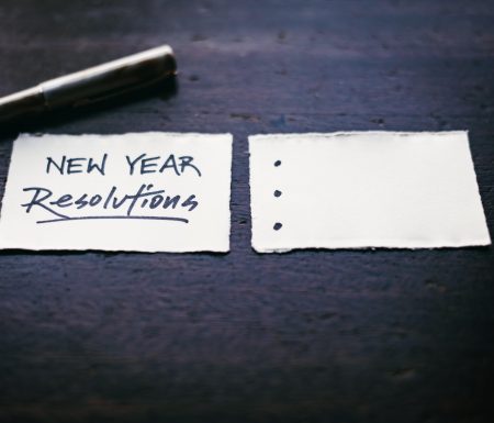 Two pieces of paper. One that says "New Year Resolutions" and the other with three bullet points