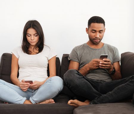 Couple sitting on couch playing on their own phones