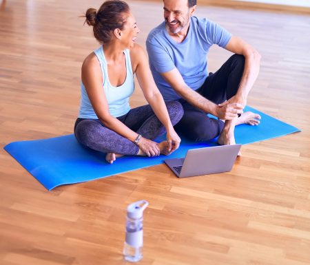 Husband and wife sitting on yoga mat watching a workout video