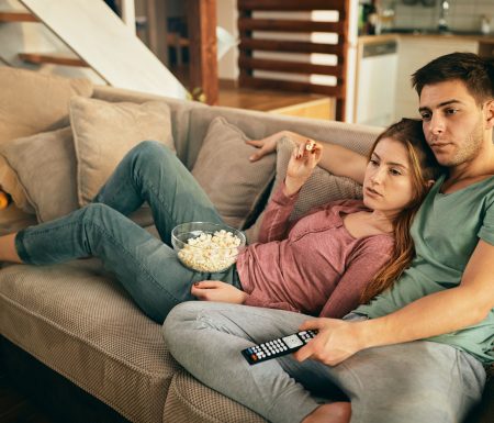 Couple relaxing on couch eating popcorn and watching tv