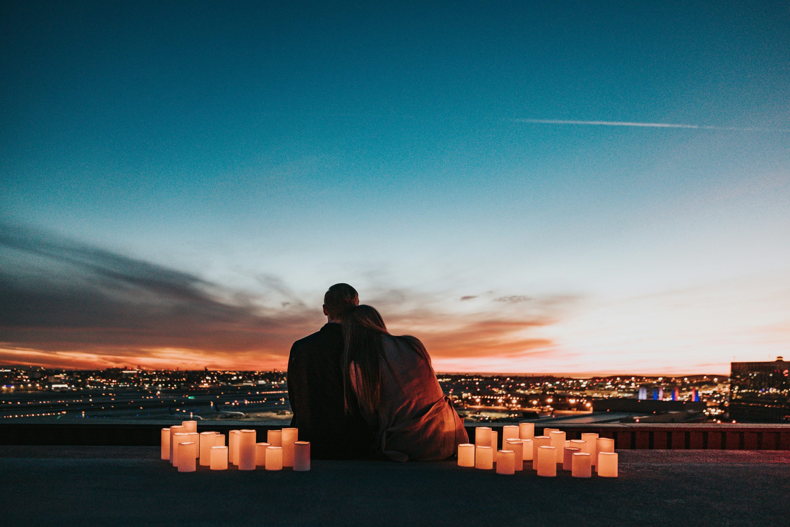 Couple sitting on rooftop overlooking city at night